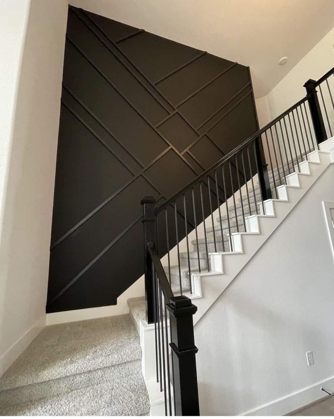 A tall, dark brown accent wall with a geometric grid pattern sits behind a carpeted staircase with a black metal railing.