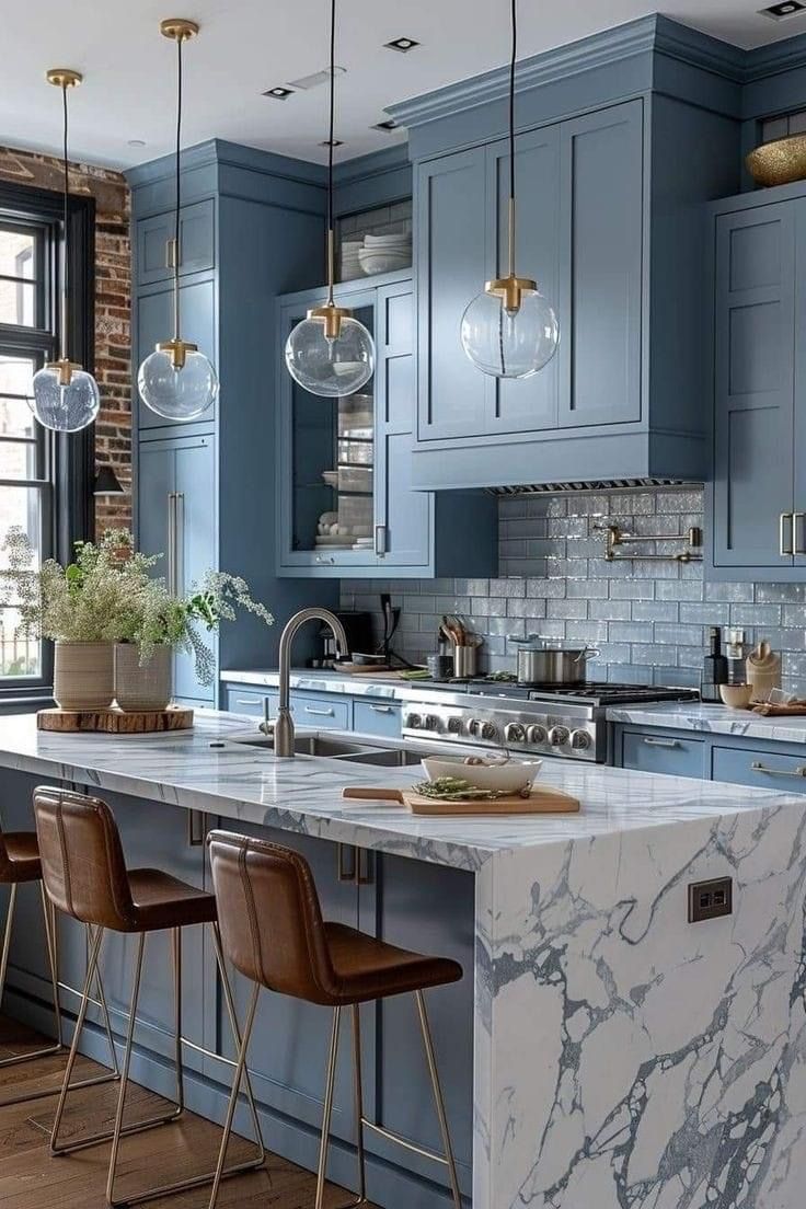 Modern kitchen with a marble waterfall island, blue cabinetry, leather bar stools, and globe pendant lighting.