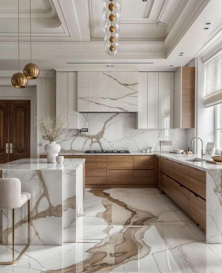 A modern kitchen with marble waterfall islands, wood cabinetry, stone backsplashes, and elegant pendant lighting.