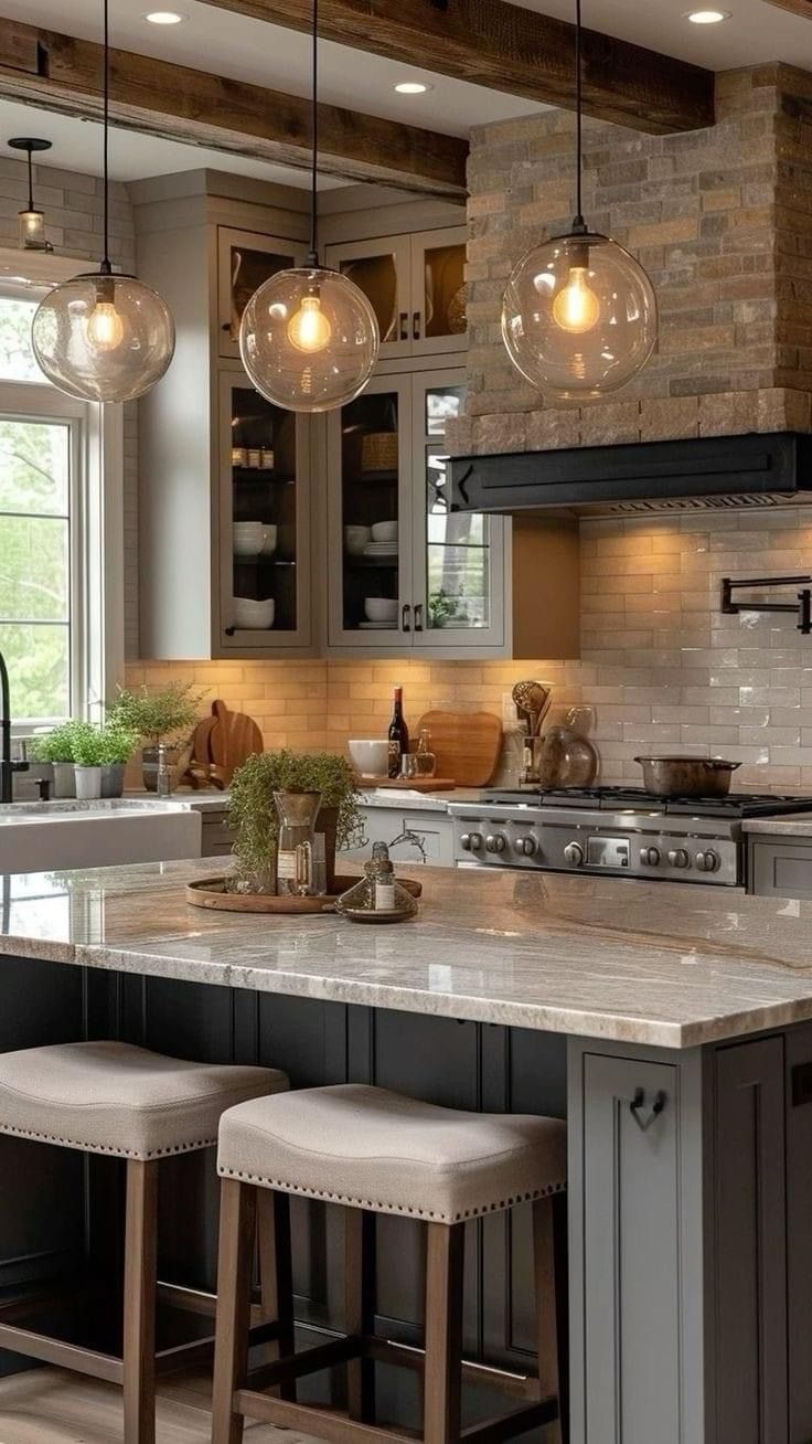 A modern kitchen with a stone-accented range hood, glass pendant lights, marble island, and gray cabinets.