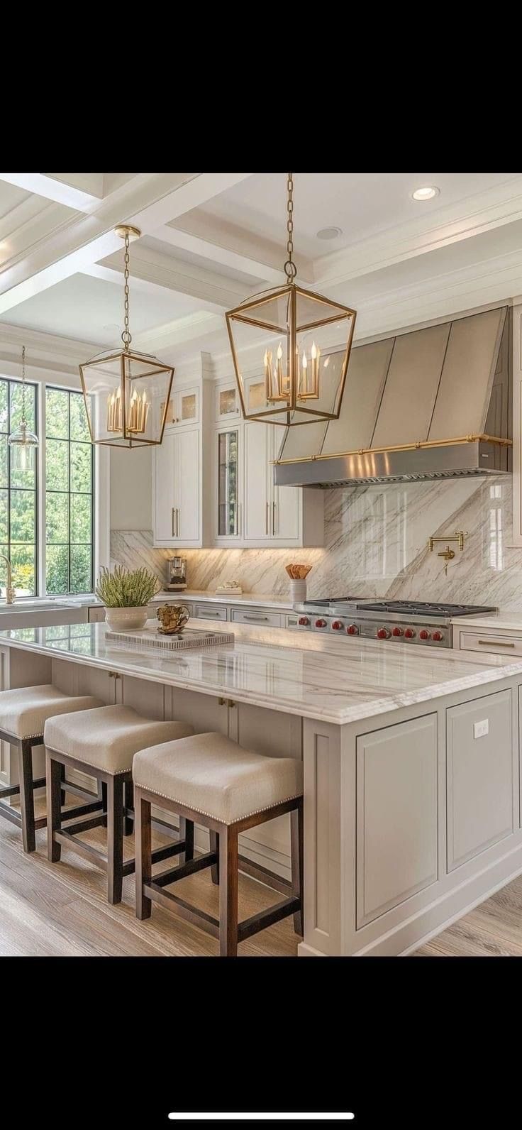 A bright, modern kitchen featuring a marble-topped island with three cushioned stools under two large lantern pendants.