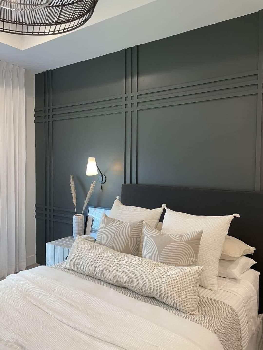 A bedroom with a dark charcoal wall featuring a grid molding design behind a bed with layered white and patterned bedding.