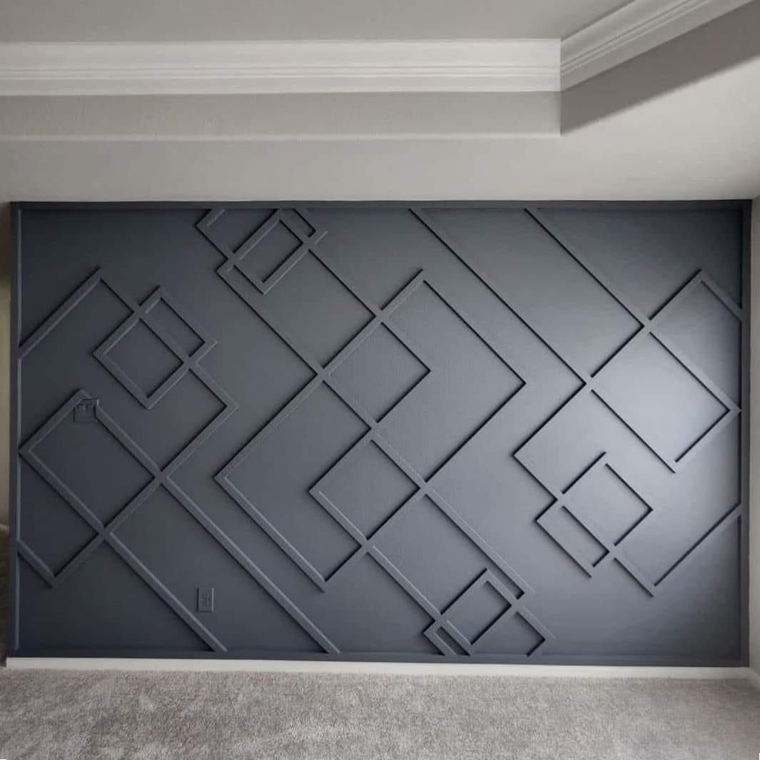 A charcoal gray wall featuring geometric molding patterns of overlapping squares and rectangles at various angles.