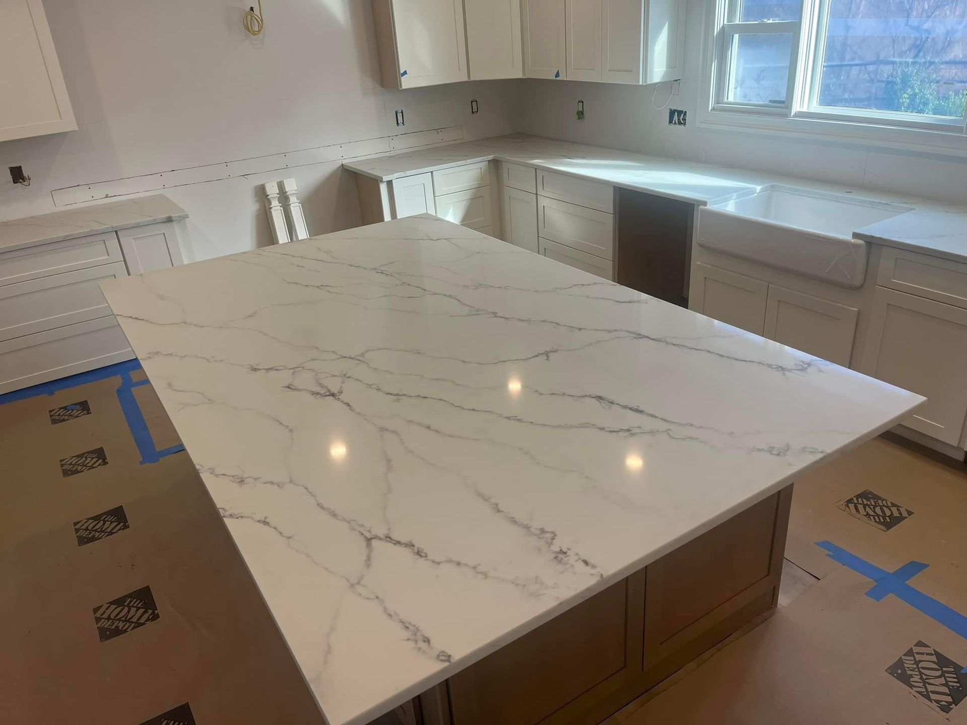 A kitchen island with a white marble-look quartz countertop and gray veining, surrounded by unfinished cabinets and floors.