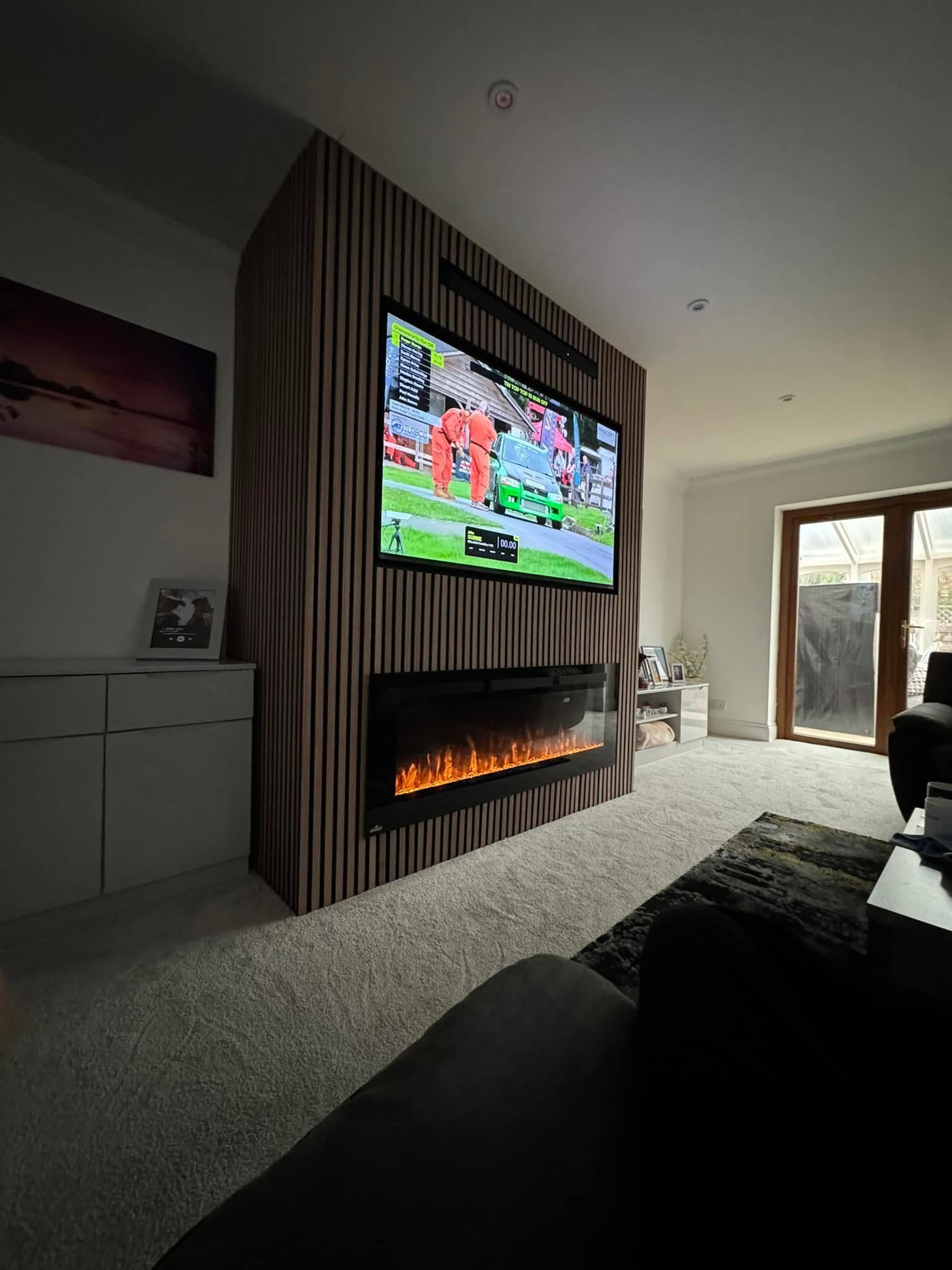 A living room with a wall-mounted TV above a linear fireplace, set against a dark, vertically-striped feature wall.