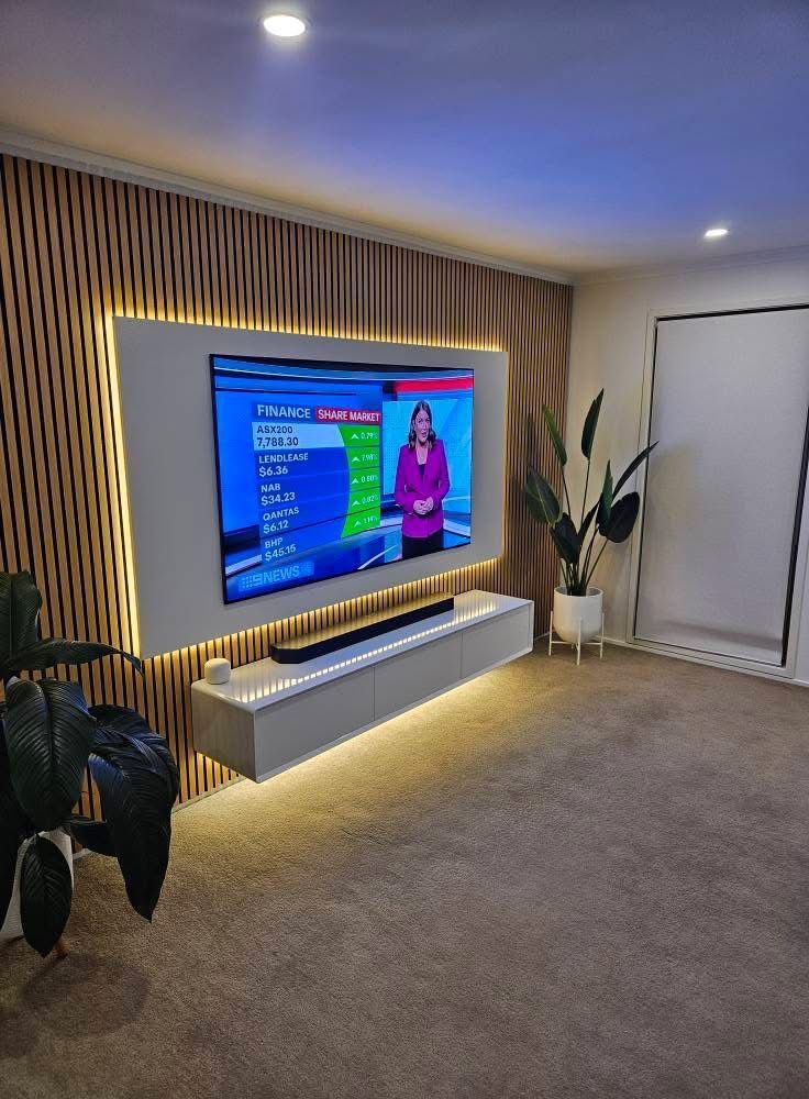 A wall-mounted TV and floating console are centered on a slatted wood wall with integrated warm ambient backlighting.