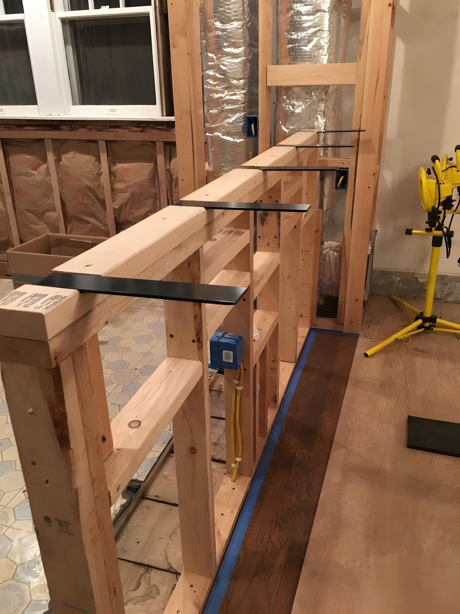 Wood framing for a bar or half-wall under construction, featuring metal countertop support brackets attached to the top.