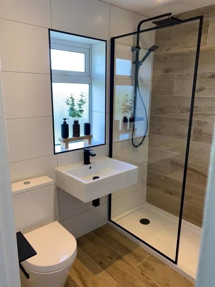 A modern bathroom with a wall-mounted sink, a toilet, and a glass-enclosed shower with wood-look tile accents.