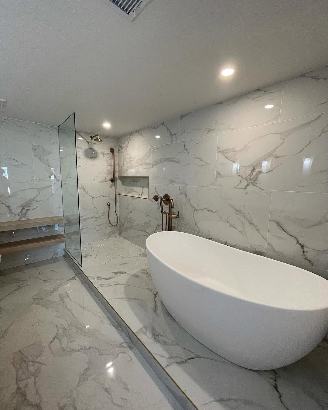 A modern bathroom featuring a white freestanding bathtub next to a glass-enclosed shower, all with marble-patterned tile.