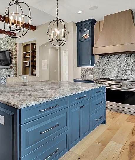 Modern kitchen with a large blue island, light granite countertops, a wood range hood, and two metal orb pendant lights.