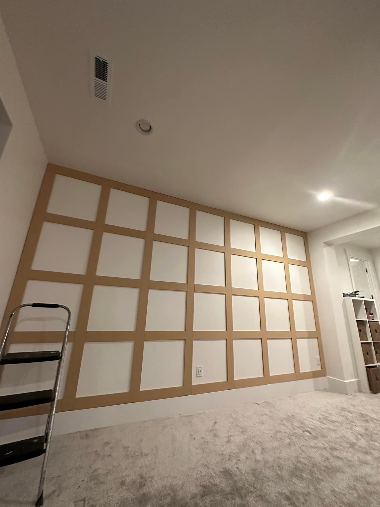 A room under construction featuring a grid-patterned wooden molding wall installation and a stepladder.