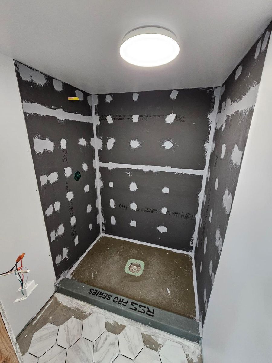 A shower stall under construction with cement backer board walls, a pre-sloped shower pan, and tiled floor outside.
