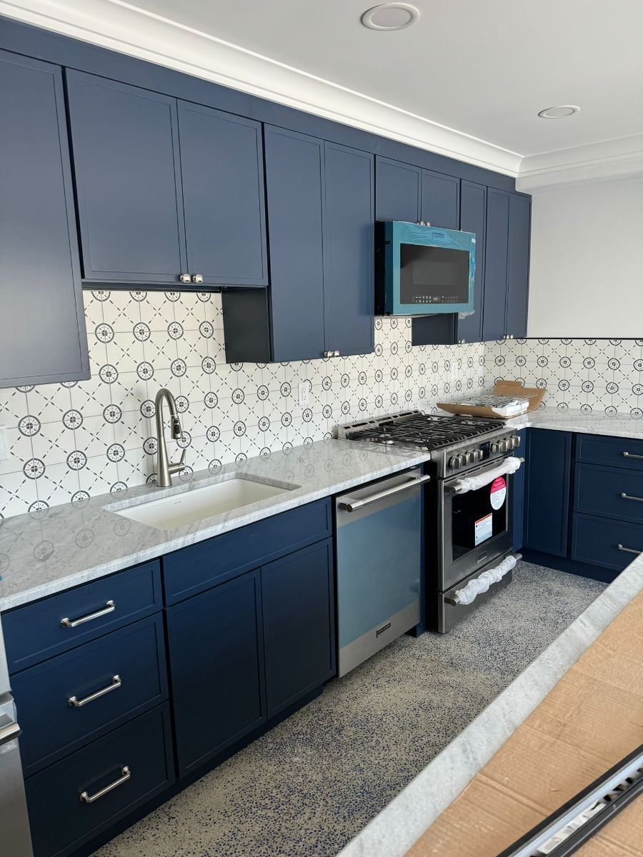 A modern kitchen featuring navy blue cabinets, white patterned tile backsplash, stainless appliances, and stone counters.