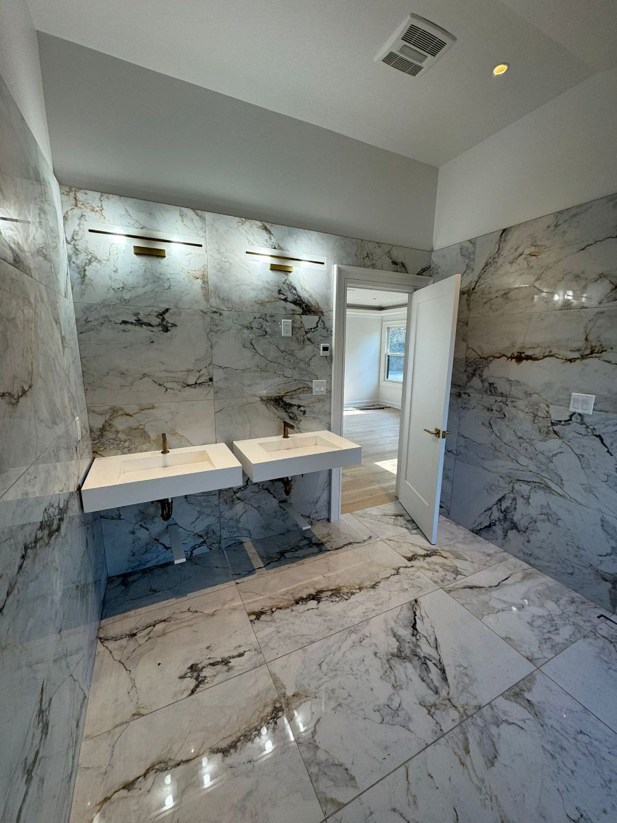 A modern bathroom featuring white marble walls and flooring, a double floating sink vanity, and an open doorway.