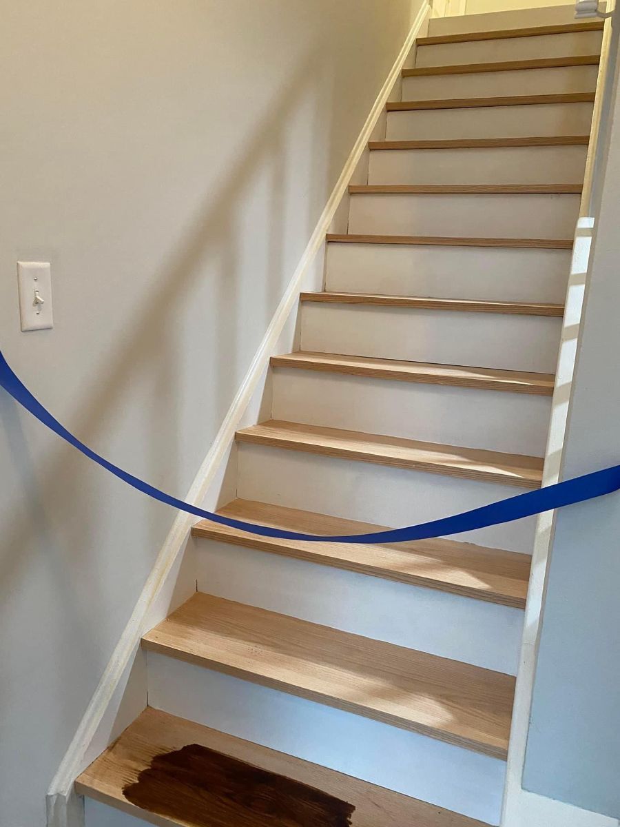 A staircase with light wood treads and white risers, blocked by a blue caution tape stretched across the lower steps.