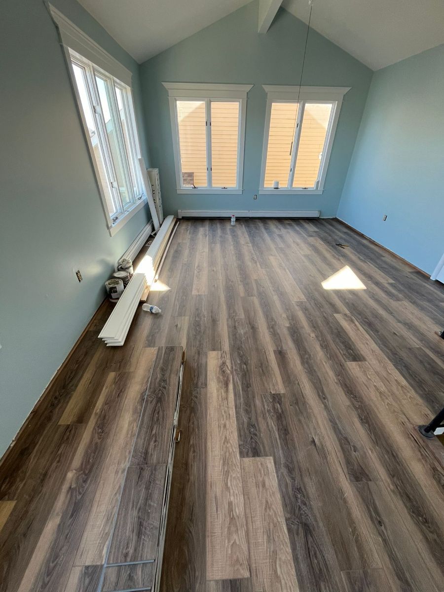 A room under renovation with new, brown wood-look plank flooring partially installed and light blue walls.