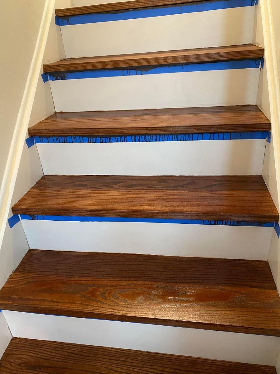 A staircase with refinished dark wood treads and freshly painted white risers, currently taped for painting.