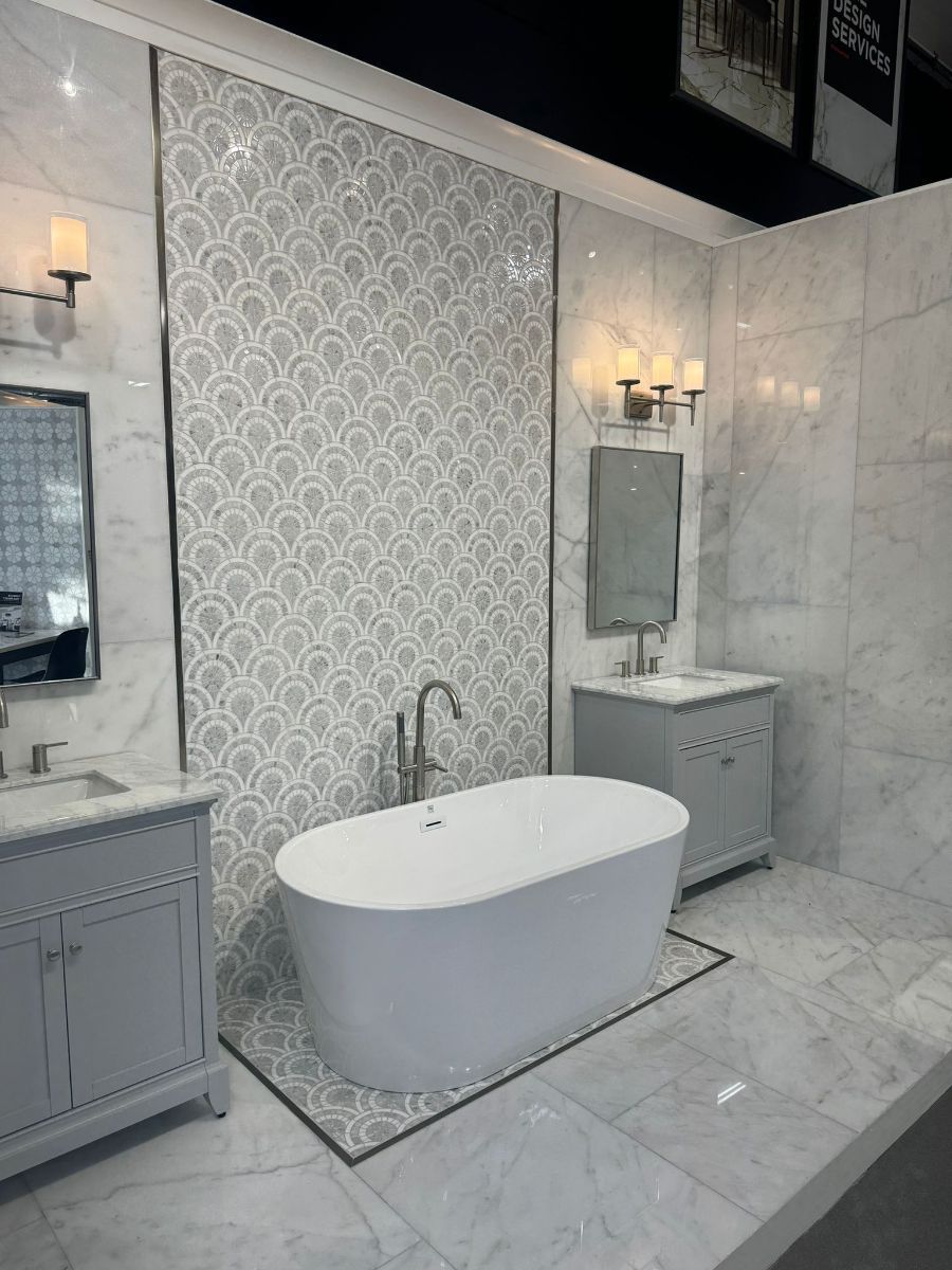 A modern bathroom featuring a white freestanding tub against a decorative fan-pattern tiled wall, flanked by two vanities.
