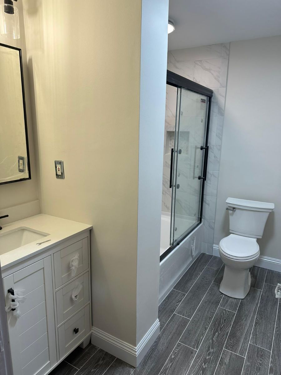 A bathroom with a white vanity cabinet, a glass-enclosed shower, a toilet, and gray wood-look tile flooring.