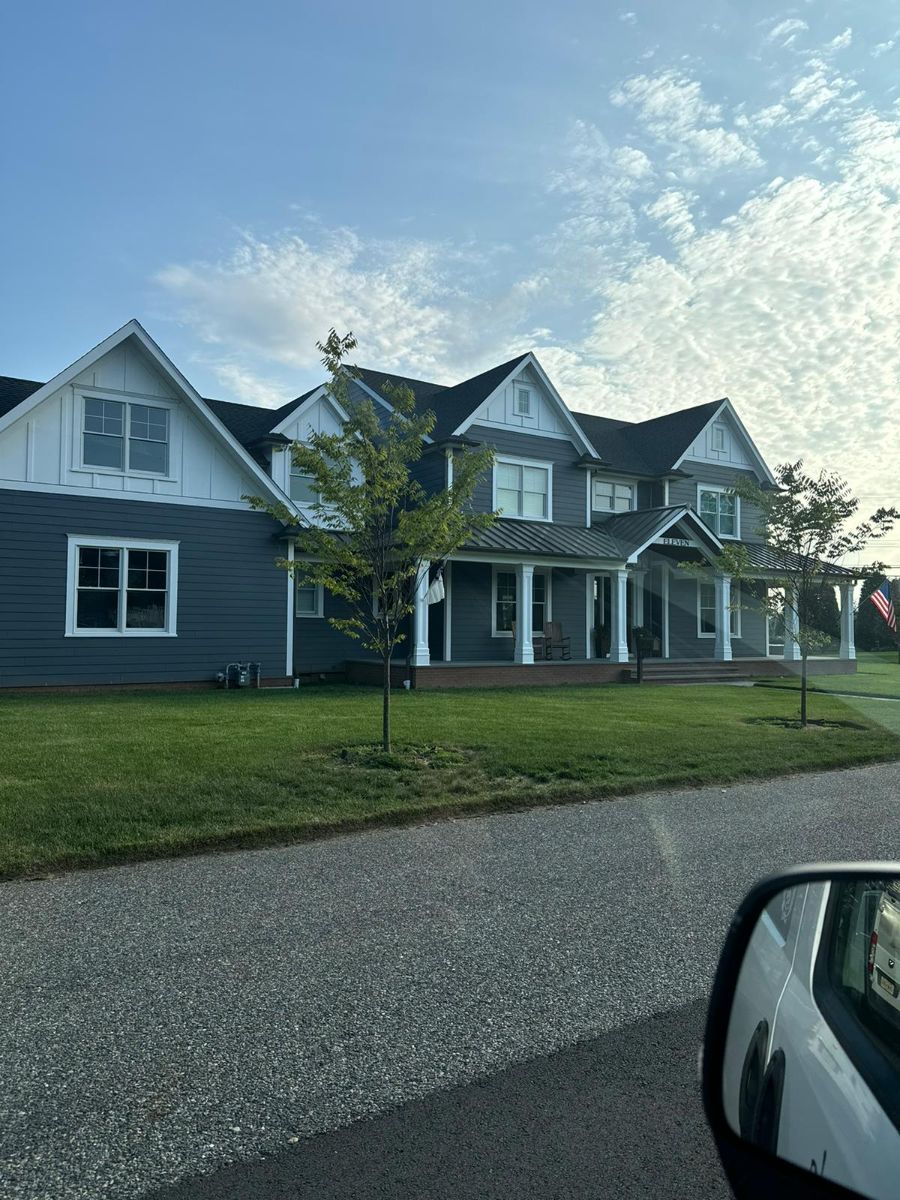 A large two-story house with blue-gray siding, white trim, and multiple gables, viewed from a gravel road.