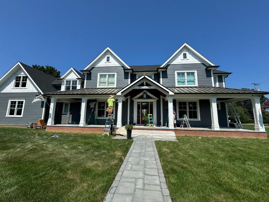 A two-story grey farmhouse with a covered porch and a stone walkway in a grassy yard, under a clear blue sky.