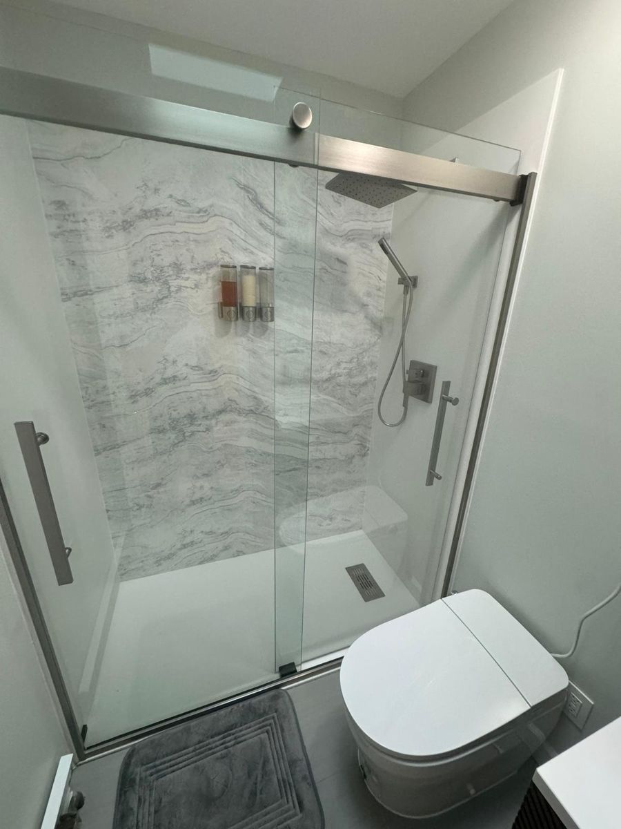 A walk-in shower with marble-patterned walls and a sliding glass door next to a white toilet in a modern bathroom.