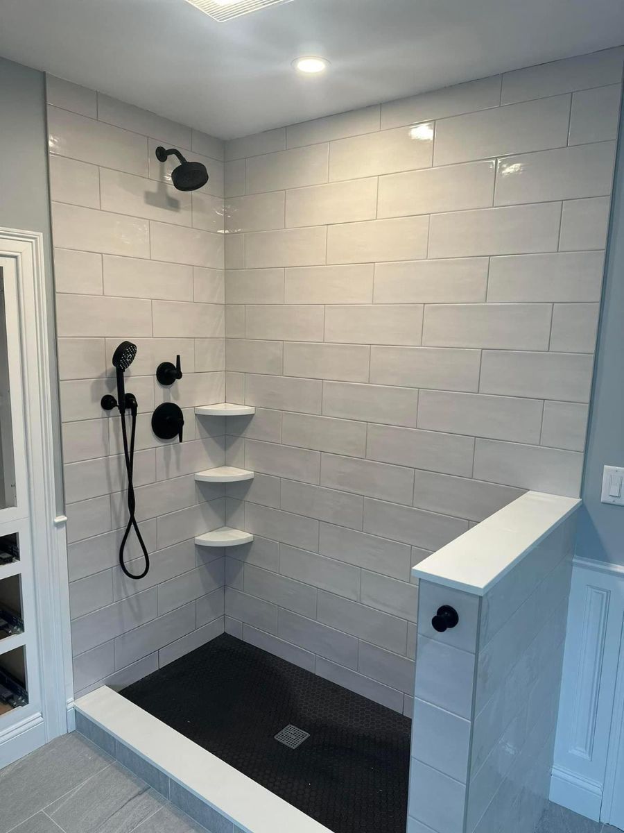 A walk-in shower with white horizontal subway tiles, a black floor, black fixtures, and built-in corner shelving.