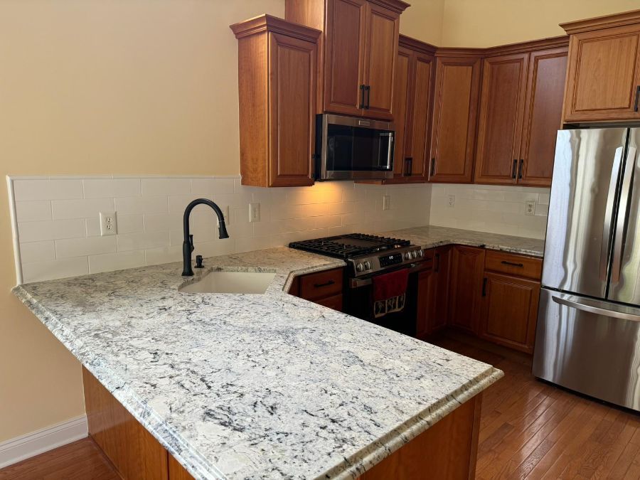 A modern kitchen with cherry wood cabinets, speckled granite countertops, a stainless steel refrigerator, and range.