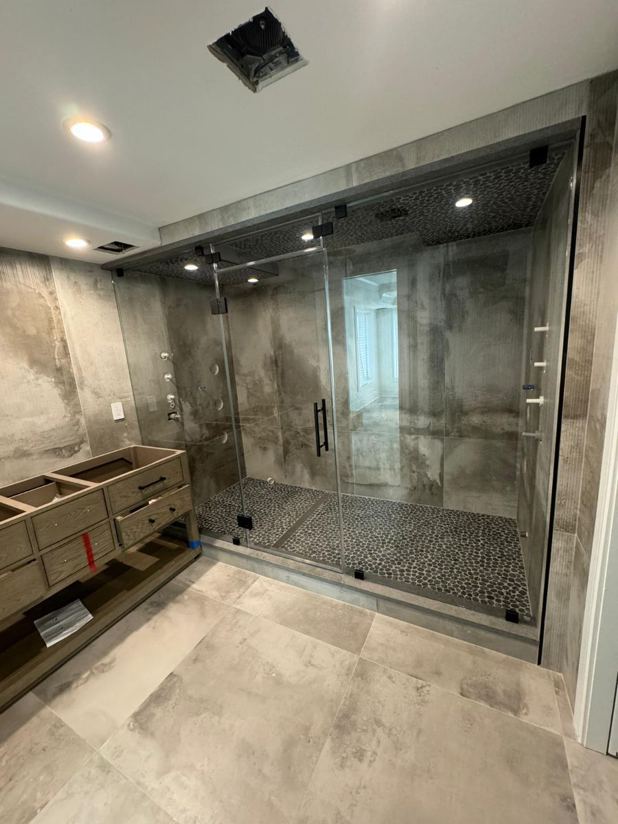 Modern bathroom featuring a large walk-in shower with stone tile, a glass door, and a partially installed wooden vanity.