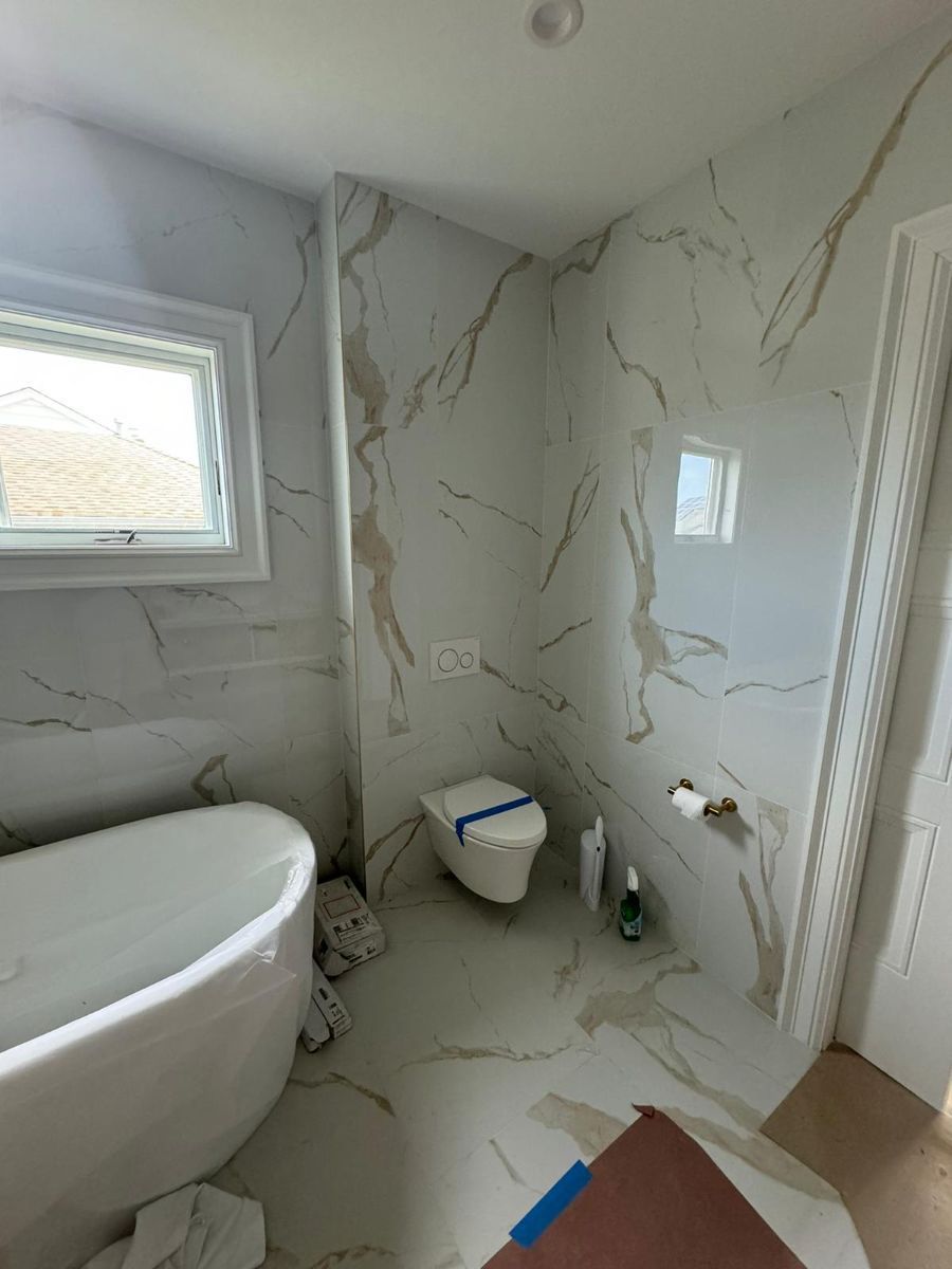 A modern bathroom featuring a white freestanding tub, a wall-mounted toilet, and large-format white marble tiles.