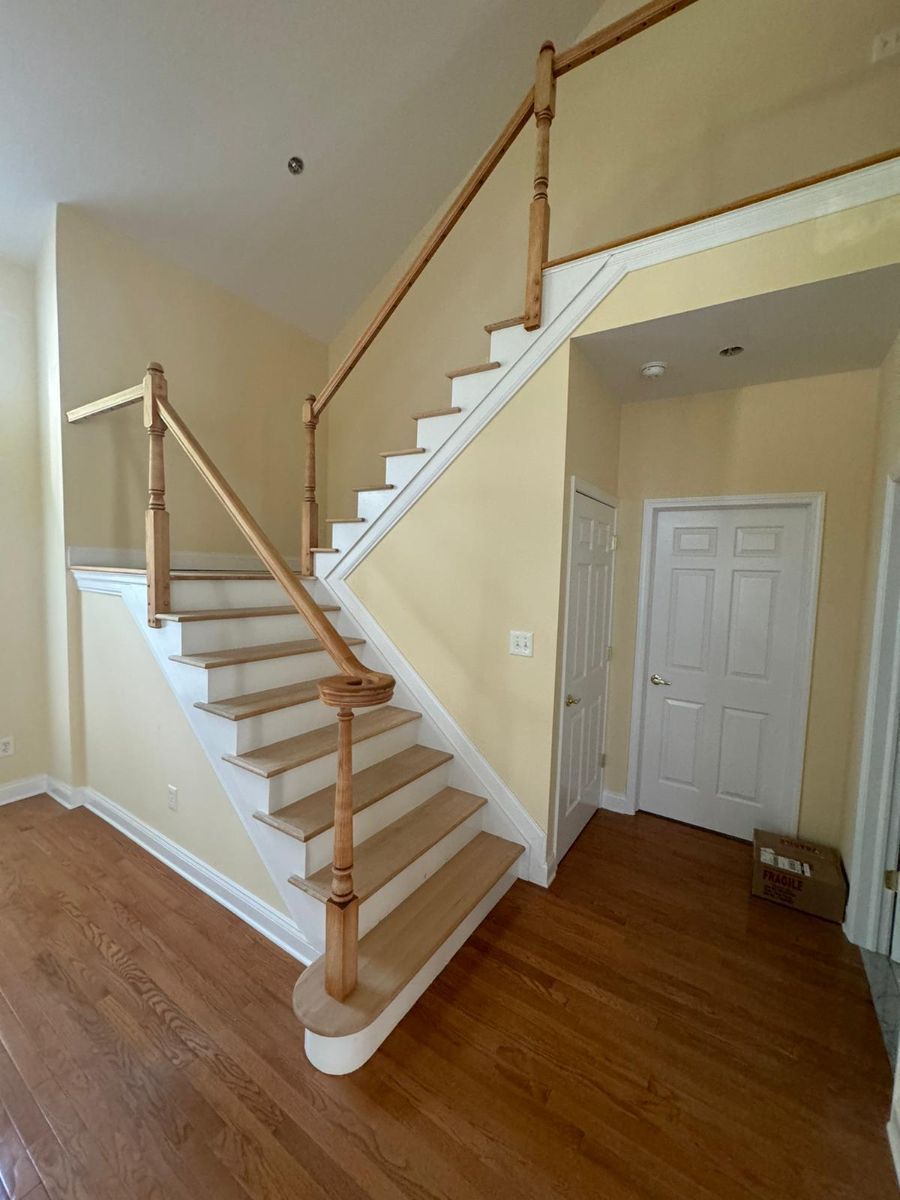A wooden staircase with white risers and a matching railing stands in a bright foyer with hardwood floors and yellow walls.