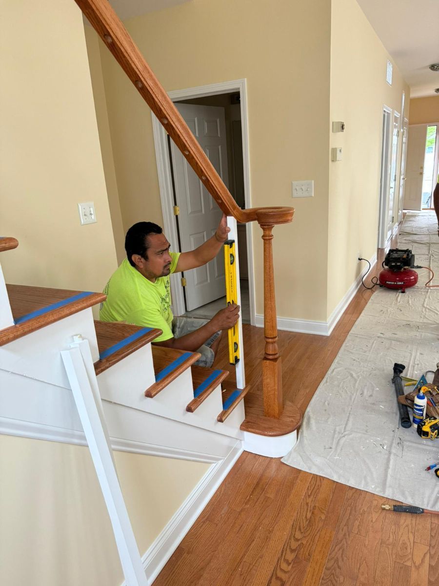 A worker in a bright yellow shirt uses a yellow level to check the vertical alignment of a wooden stair baluster.
