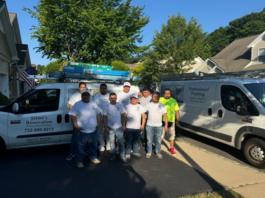 A group of nine workers in matching white shirts stand between two white service vans parked on a residential street.