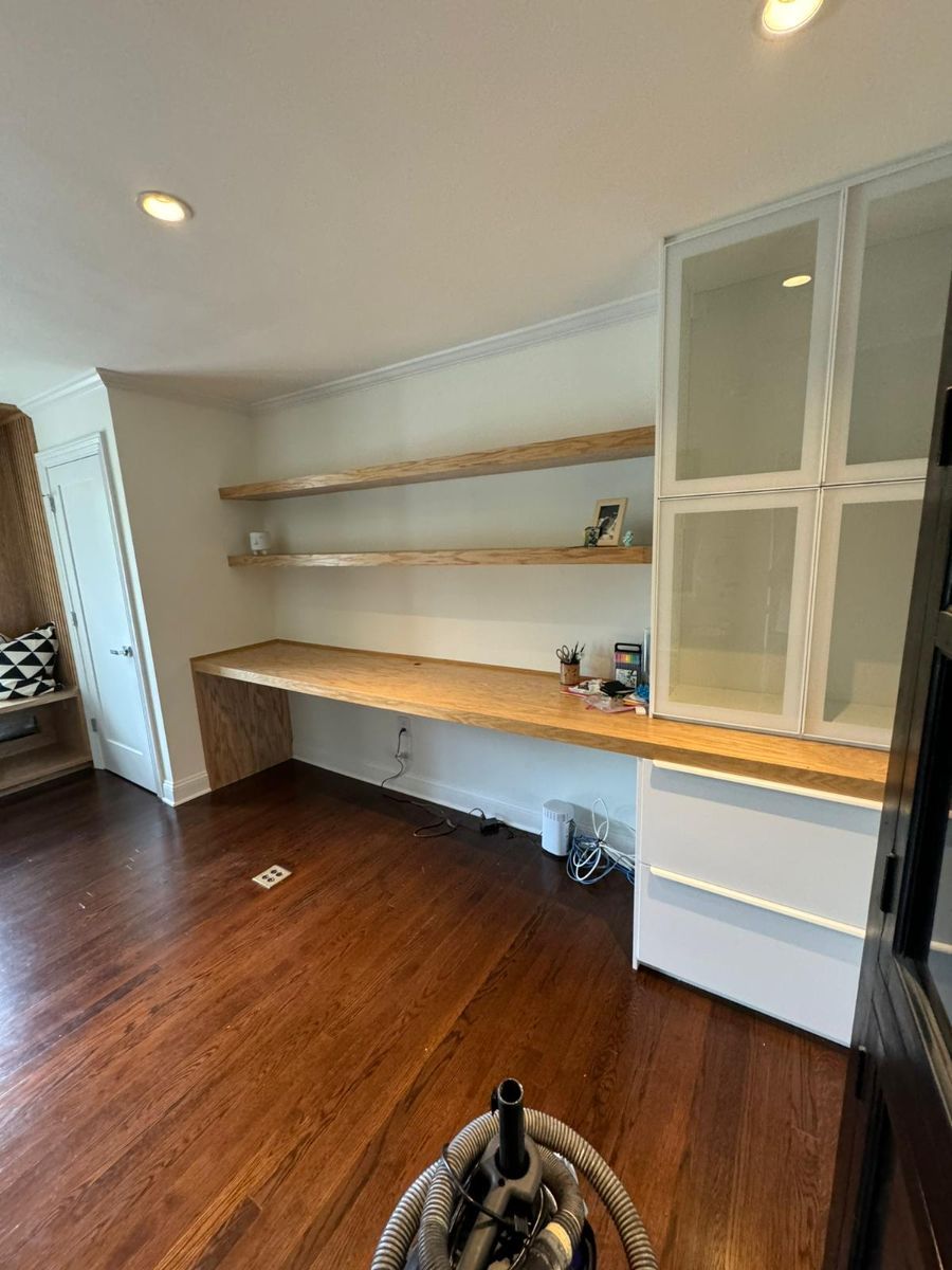 A desk area with a wood countertop, two matching floating shelves, and a white built-in cabinet against a white wall.