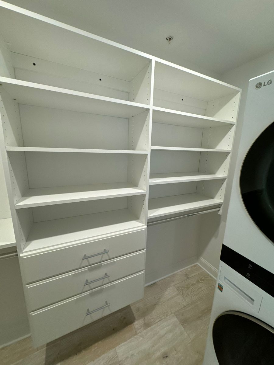 White built-in closet shelving with three lower drawers next to a white stacked washer and dryer unit.