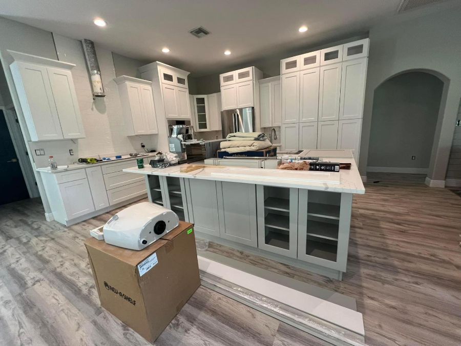 A spacious, modern white kitchen with an island, light wood-look floors, and a cardboard box in the foreground.