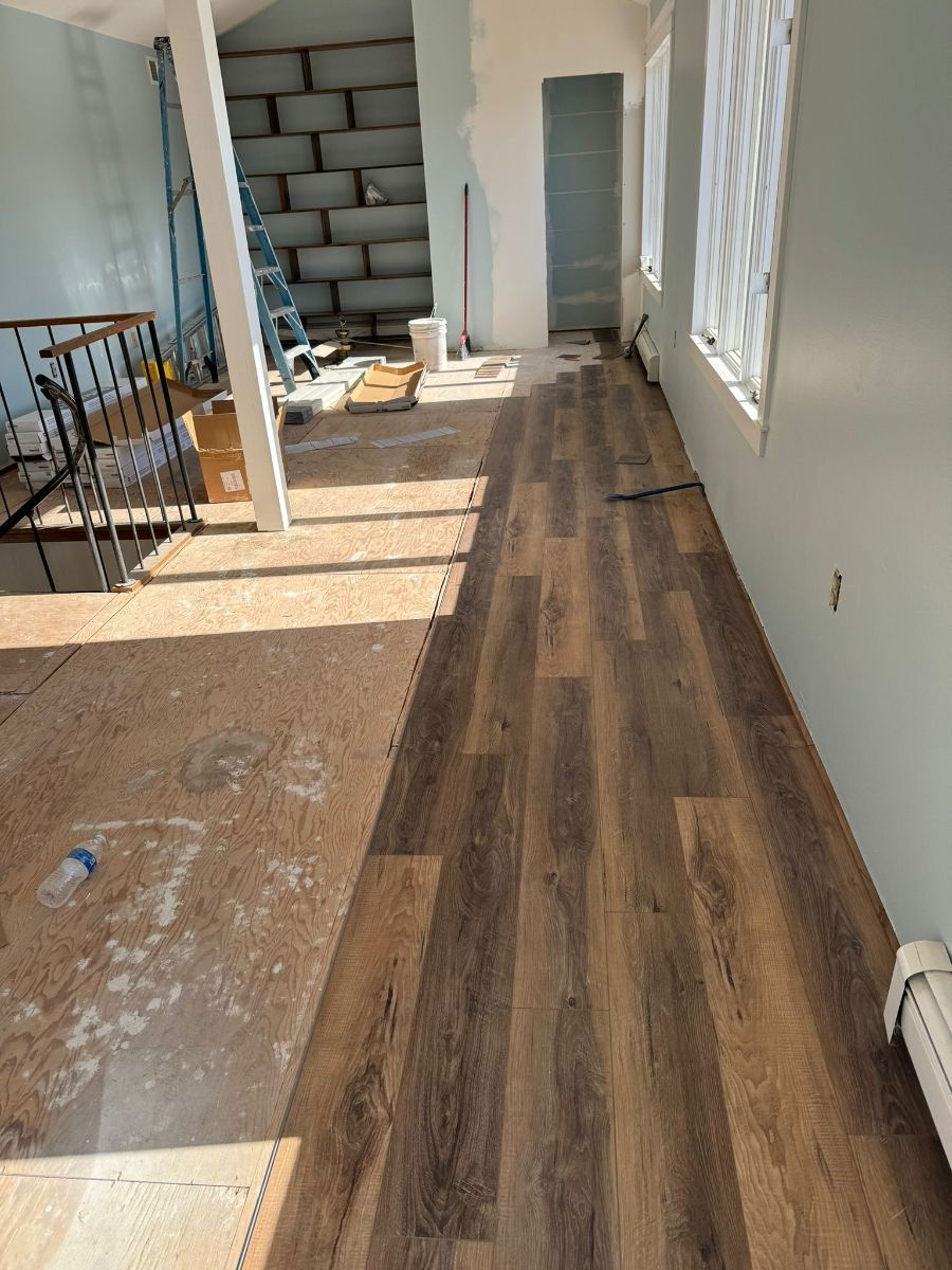 A room undergoing renovation with partially installed dark wood-look plank flooring and exposed subflooring.