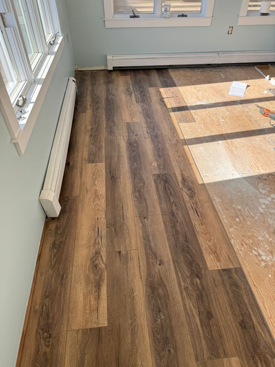 New wood-look laminate flooring being installed in a room with light blue walls and a white baseboard heater.