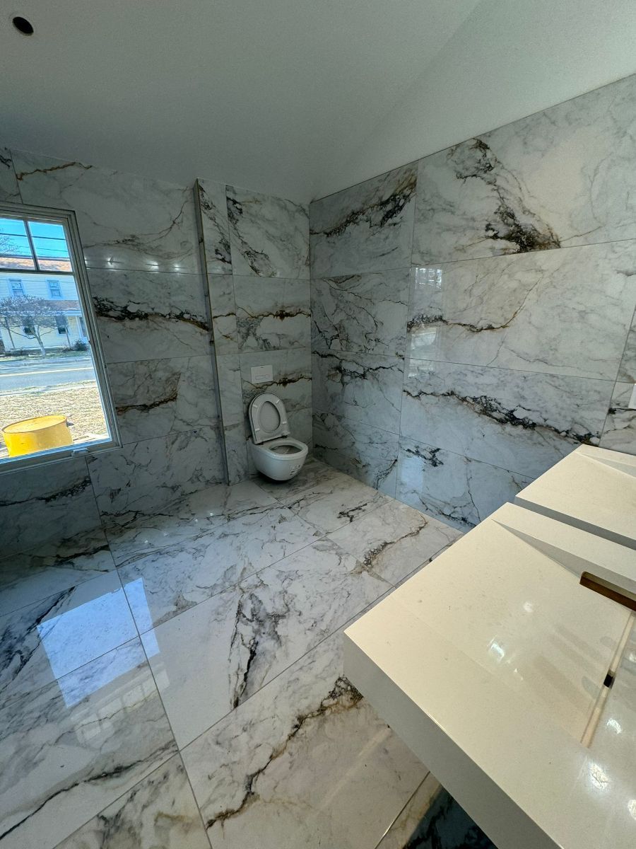 A modern bathroom featuring grey and white marble tiles on the walls and floor, a wall-mounted toilet, and a vanity counter.
