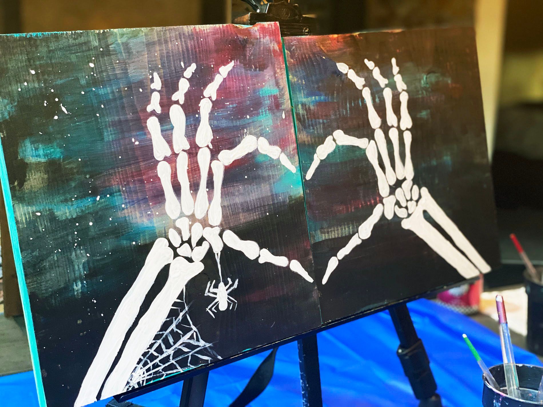 Two paintings of skeleton hands making a heart shape on an easel.