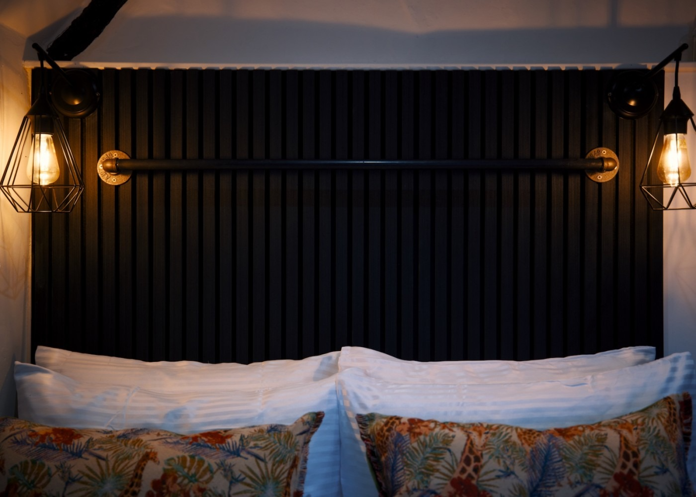 Bed headboard with vertical black slats, two hanging lamps, and pillows.