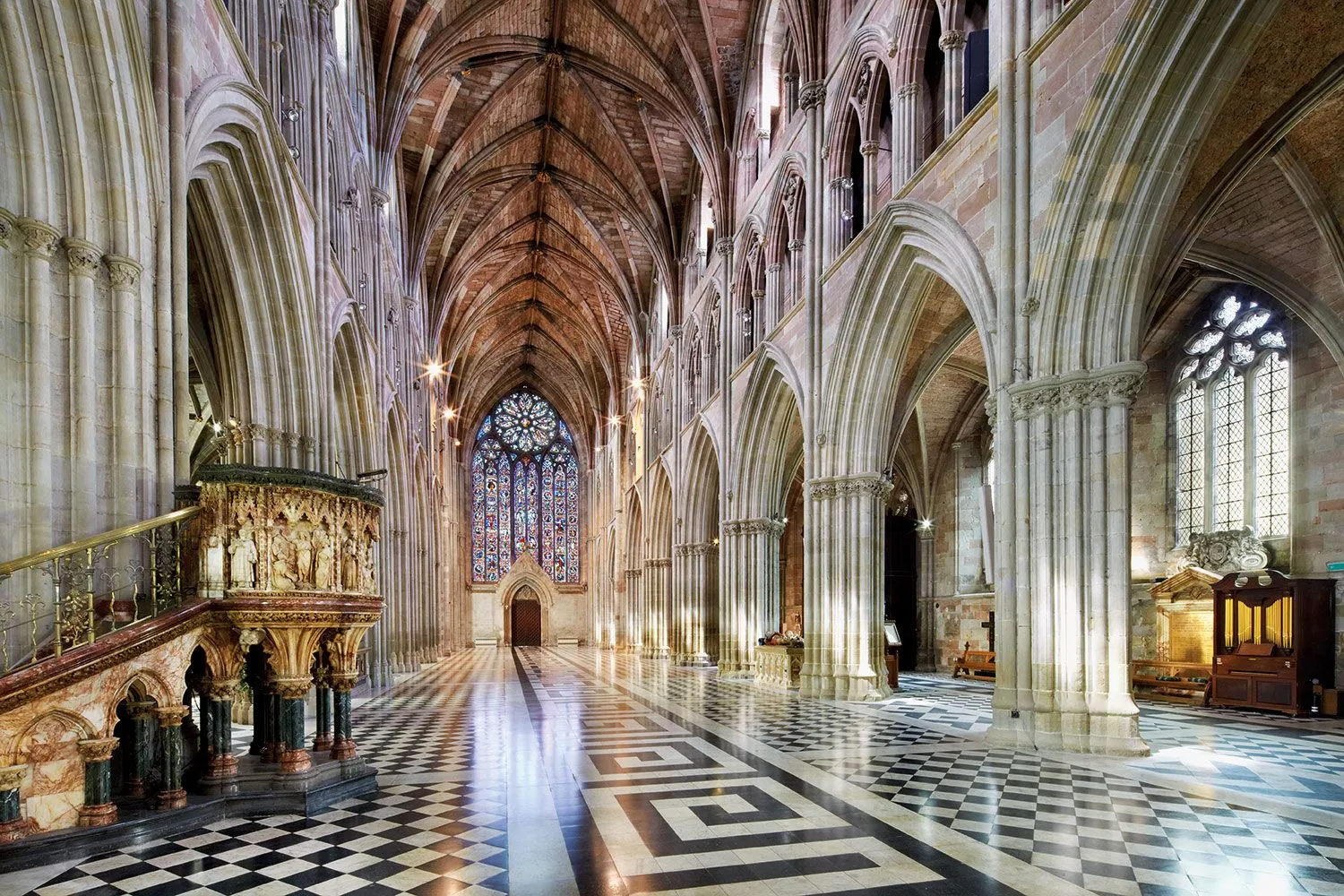 Interior view of a cathedral with Gothic architecture, black and white tiled floor, and stained glass windows.