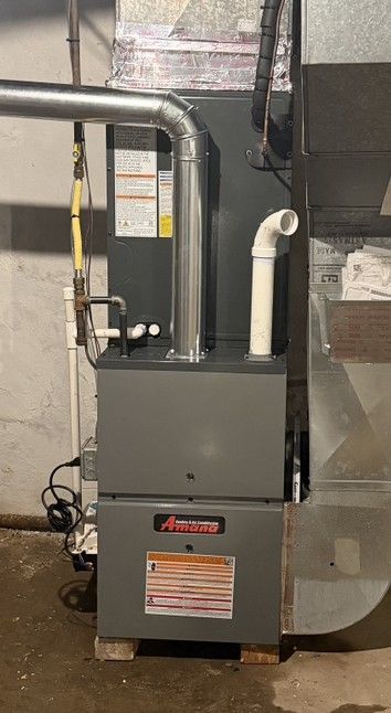 Gray furnace and HVAC ductwork in a utility room, with pipes and a filter label visible.