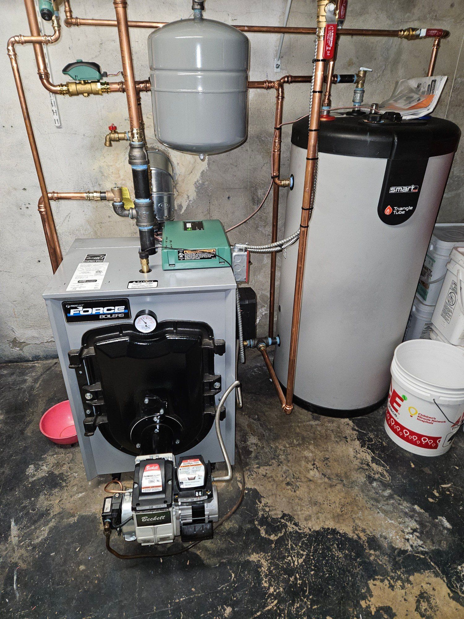 Basement boiler and water heater setup with copper pipes, tanks, and pump assembly