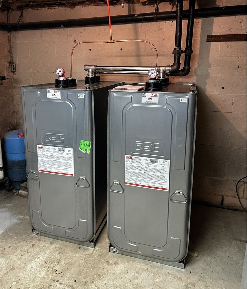 Two gray water heaters in a basement beside exposed pipes and a concrete wall