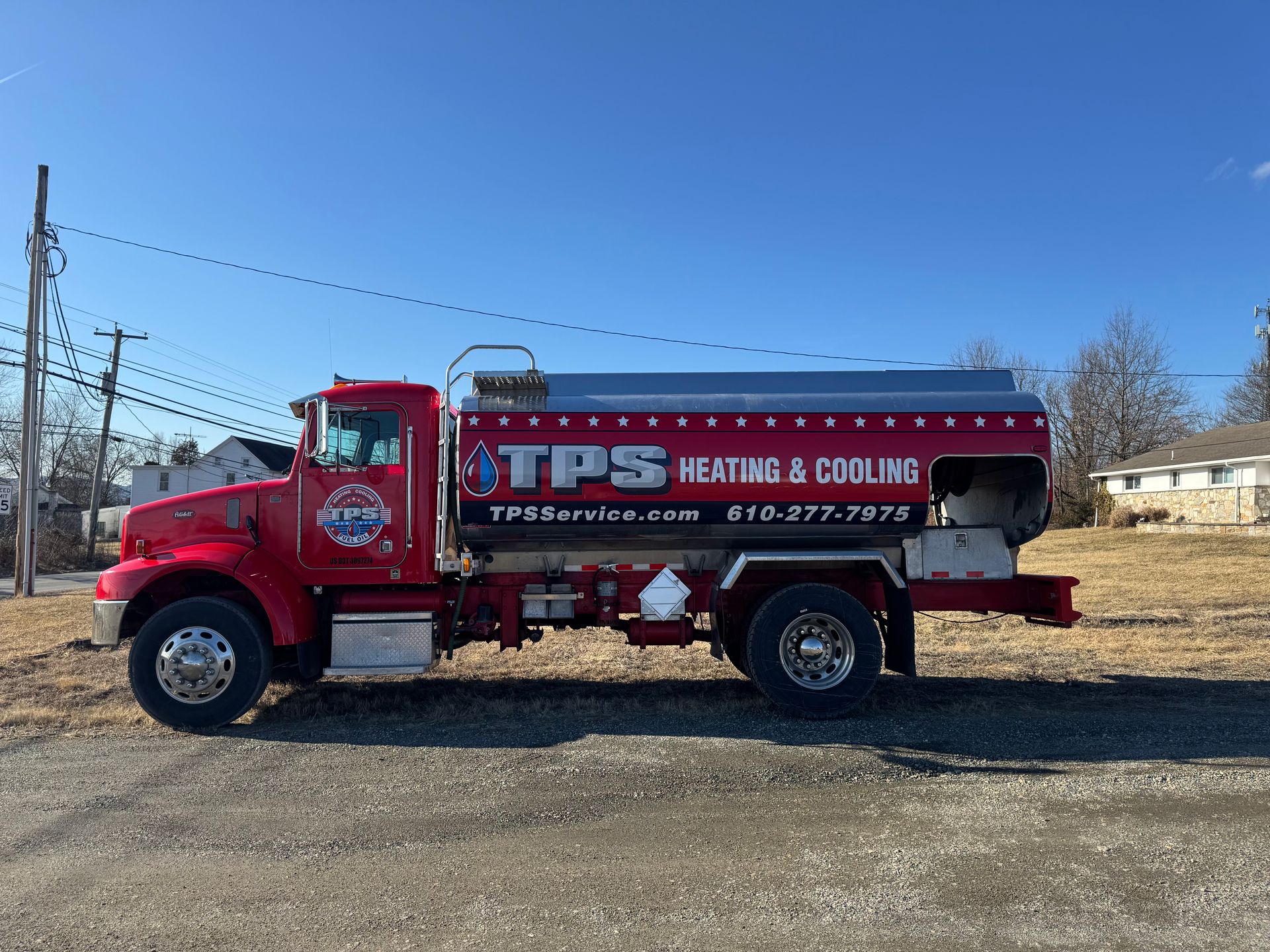 Red water truck with “TPS Heating & Cooling” parked on a gravel lot under a blue sky.