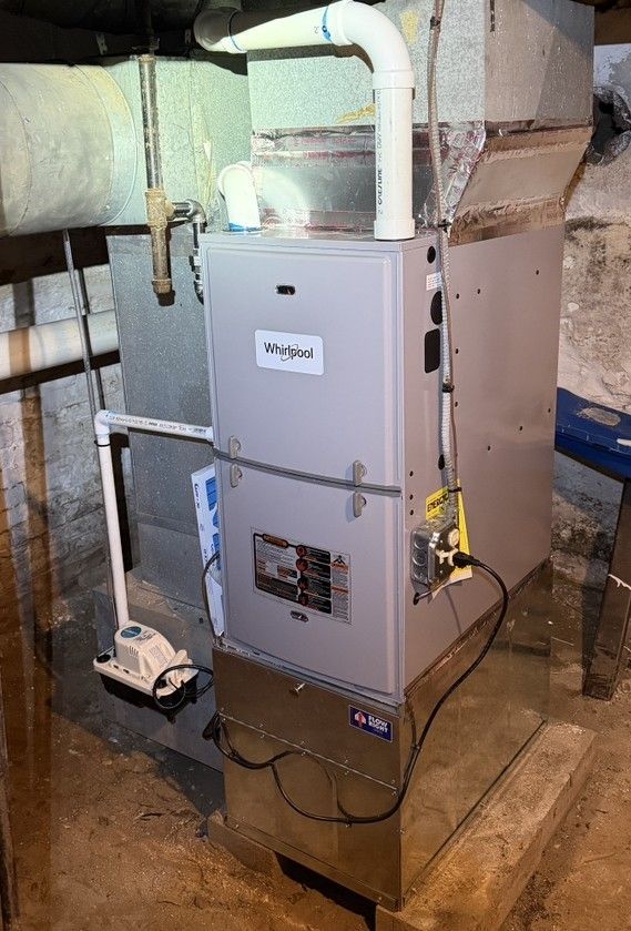 Gray furnace/air handler in a basement utility room with exposed pipes and vents.