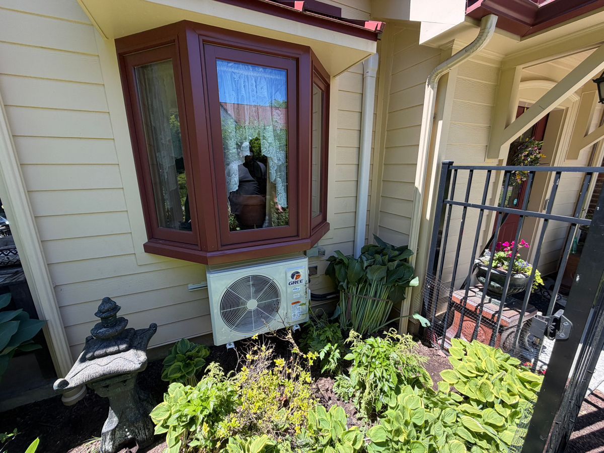 House exterior with bay window, air conditioner, and garden plants beside a black gate