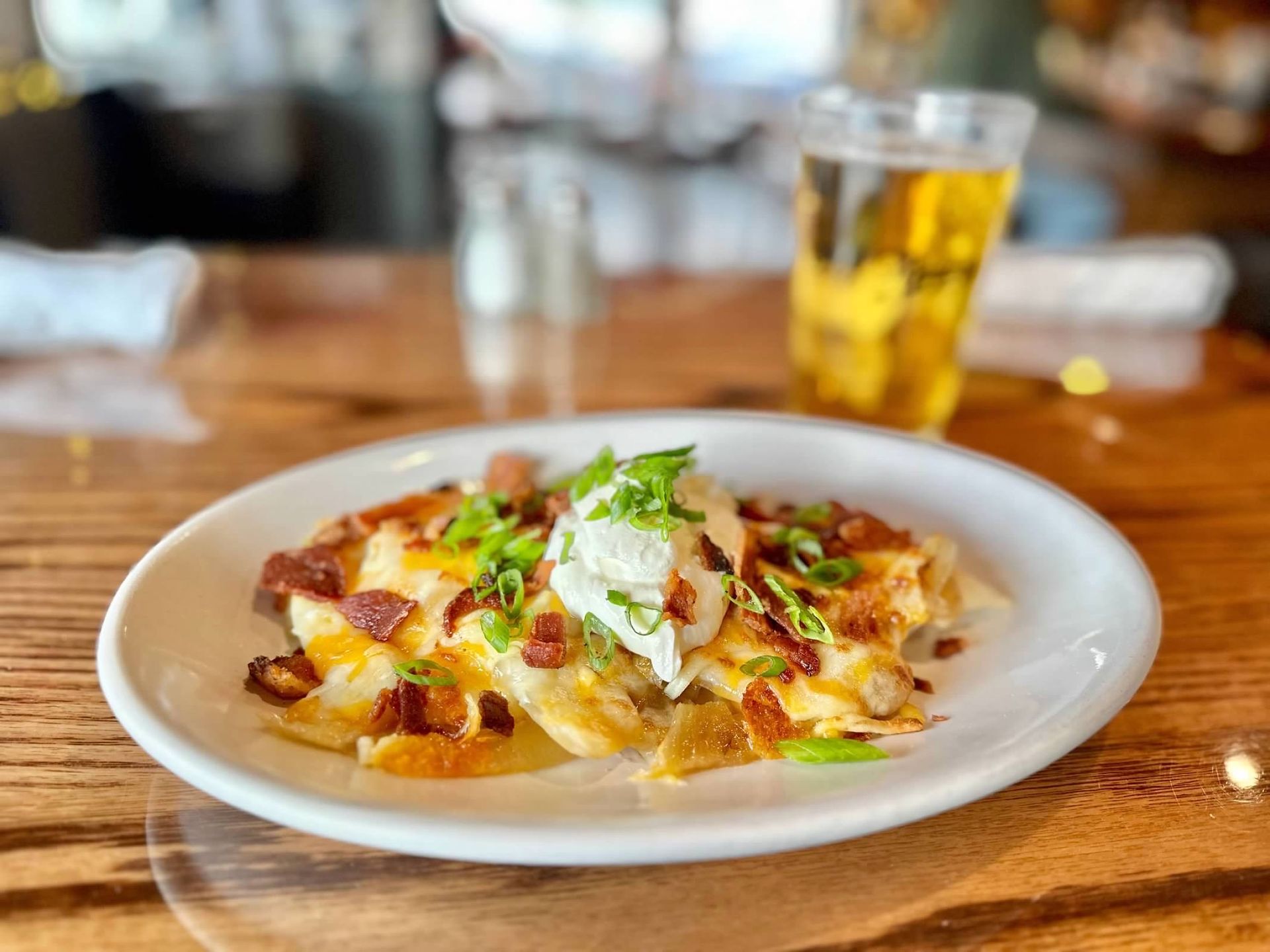 A plate of loaded potato skins topped with melted cheese, bacon, sour cream, and scallions next to a glass of beer.