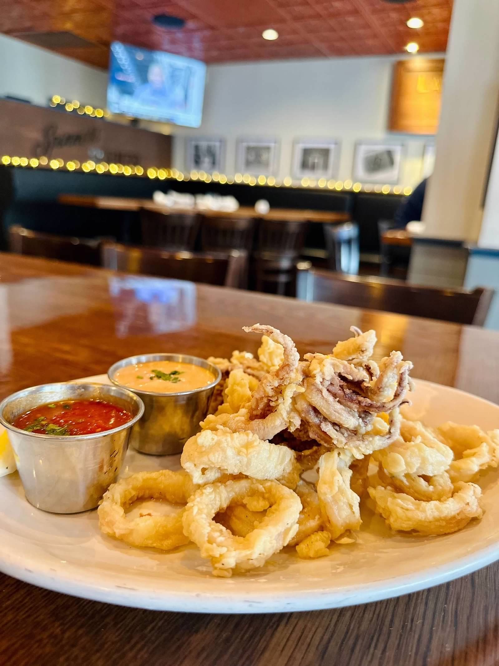 A plate of fried calamari served with red marinara and a creamy dipping sauce, set on a wooden table in a restaurant.